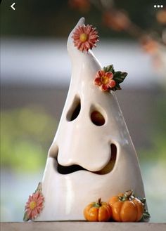 a white vase with flowers on it sitting on a table next to some pumpkins