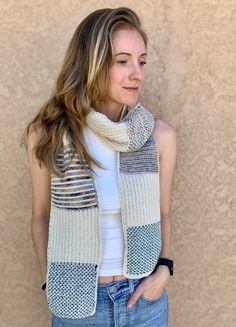 a woman wearing a scarf and jeans standing in front of a wall with her hands on her hips