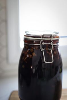 a glass jar filled with liquid sitting on top of a wooden table next to a window