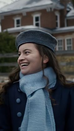 a woman wearing a hat and scarf standing in front of a house