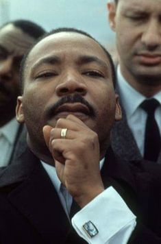 a man in a suit and tie holding his hand to his face with other men standing behind him