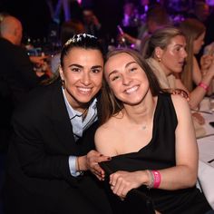 two women sitting next to each other at a dinner table with people in the background