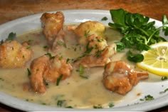 a white plate topped with shrimp covered in gravy next to a lemon wedge