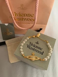 a white bracelet with gold clasps and pearls in front of a pink shopping bag