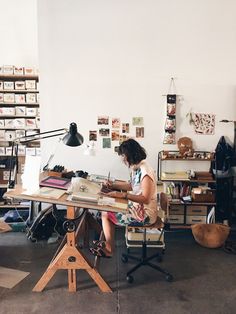 a woman sitting at a desk working on a piece of paper in an art studio