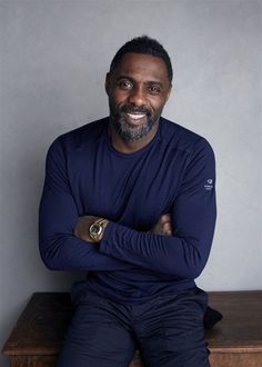 a man with his arms crossed sitting on a wooden bench in front of a gray wall