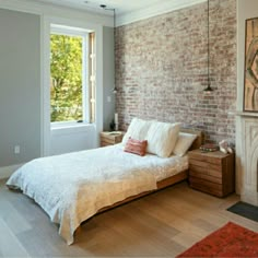 a bedroom with a brick wall and white bed in the corner, next to a fireplace