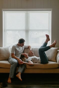 a man and woman sitting on top of a couch next to each other in front of a window