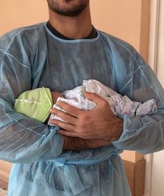 a man in scrubs holding a baby and looking at the camera while standing next to a sink