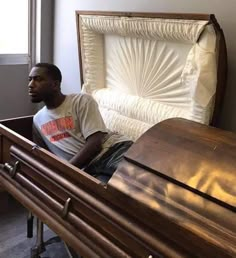 a man sitting in a wooden casket next to a window with white sheets on it