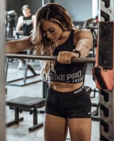 a woman is doing squats on a bar in the gym with her hands behind her back