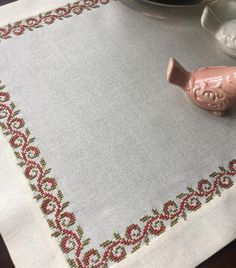 a table topped with a pink bird next to a cup and saucer on top of a white cloth