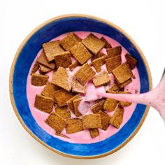 a blue bowl filled with pink yogurt and toast croutons next to a spoon