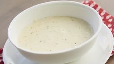 a bowl of soup sitting on top of a white plate next to a red and white napkin