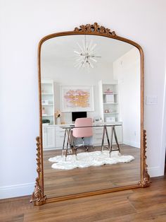 a large gold mirror sitting on top of a hard wood floor next to a desk