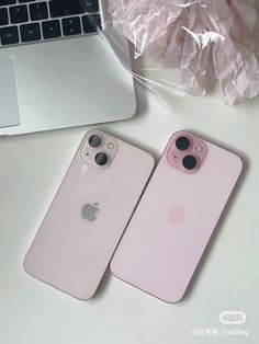 two pink iphones sitting next to each other on top of a white table near a laptop