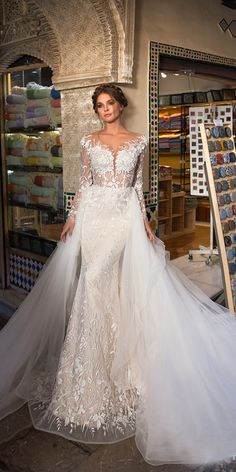 a woman standing in front of a store wearing a wedding dress with long sleeves and sheer tulle