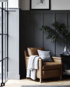 a living room with black paneling and leather chair next to a potted plant