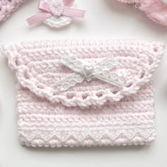 a crocheted pink purse with white lace and bows on the front, surrounded by other crochet items