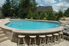 an above ground swimming pool surrounded by stone steps and seating area with stools next to it