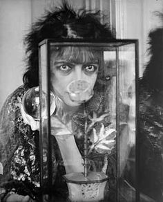 an old photo of a woman holding a flower in front of her face and looking through a glass case