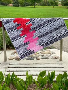 a pink and black quilt hanging from a metal rail in front of some green grass