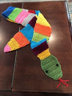 a crocheted fish is laying on the floor next to a piece of wood