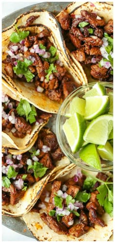 several tacos with meat, onions and cilantro on a plate next to lime wedges