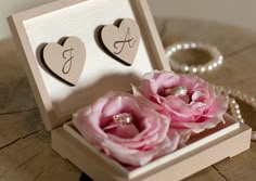 two wedding rings in a box with pink flowers on a table next to pearls and necklaces