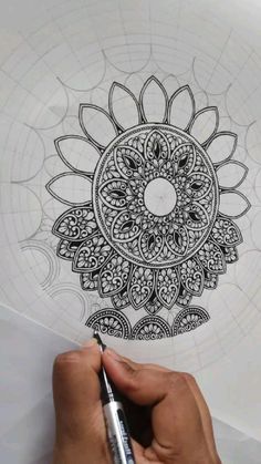 someone is drawing an intricate flower design on paper with a marker and pen in their hand