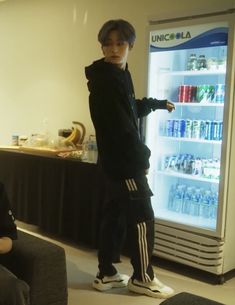 a man standing in front of a refrigerator with drinks on it's shelves and people sitting around