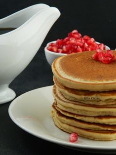 a stack of pancakes sitting on top of a white plate next to a bowl of pomegranates