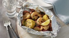 shrimp, corn and potatoes in foil on a wooden plate with silverware next to it