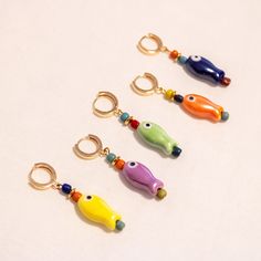 four different colored fish shaped keychains on a white surface with gold rings and hooks