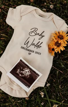 a baby's bodysuit is laying on the grass next to a sunflower