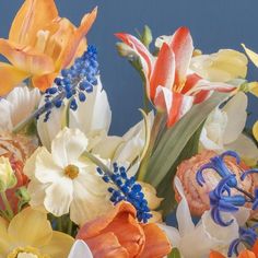 an arrangement of flowers with blue stems and orange, white, and yellow flowers in the background