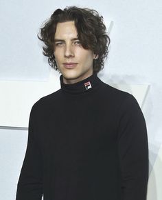 a man with curly hair wearing a black turtle neck sweater