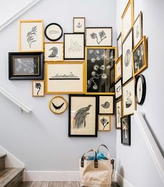 a bunch of pictures hanging on the wall next to a stair case with a handbag