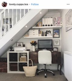 a computer desk sitting under a stair case next to a wall mounted tv and bookshelf