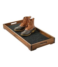 a pair of brown boots sitting on top of a black mat in a wooden tray