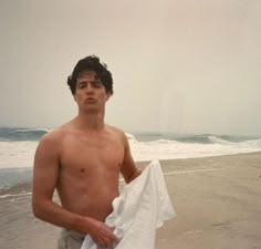 a shirtless man holding a white towel on the beach