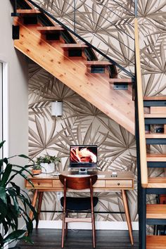 a wooden desk sitting under a stair case next to a table with a laptop on it