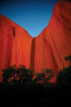 the sun is setting on an orange rock formation, with trees in front of it