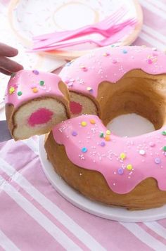 a pink frosted donut on a plate with a slice taken out of it