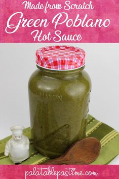 a jar filled with green poblaano next to a wooden spoon on top of a table