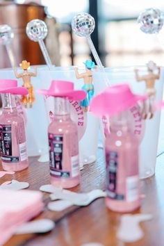 some pink bottles and spoons sitting on a table with confetti in them