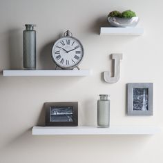 two white shelves with pictures and an alarm clock on one side, another shelf has a small potted plant