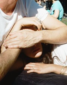 a man and woman sitting next to each other in the grass with their arms around one another