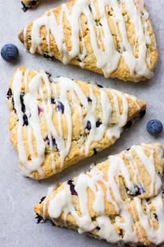 three blueberry scones with icing and fresh blueberries on the side next to each other