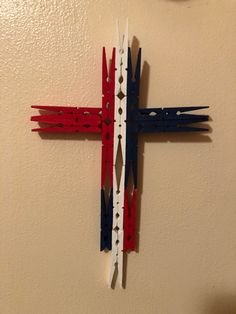 a wooden cross with red, white and blue strips on it hanging from the wall